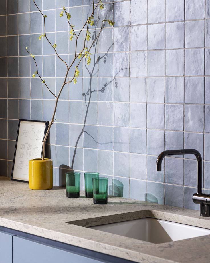 a kitchen sink with green glasses and a vase on the counter top next to it