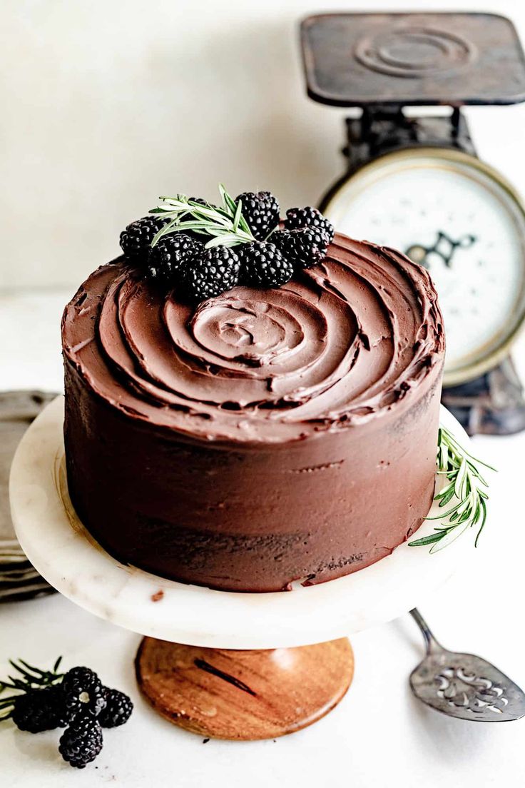 a chocolate cake sitting on top of a white plate next to a clock and other kitchen utensils