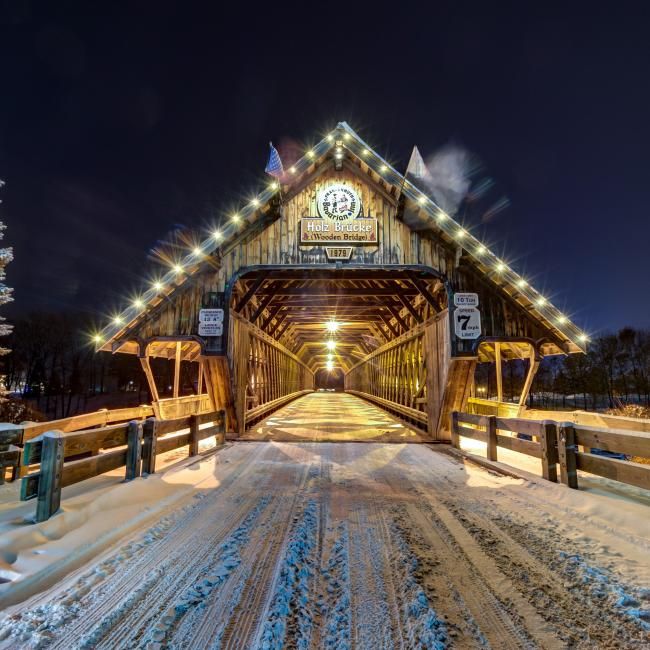 a covered bridge at night with snow on the ground and lights in the sky above it