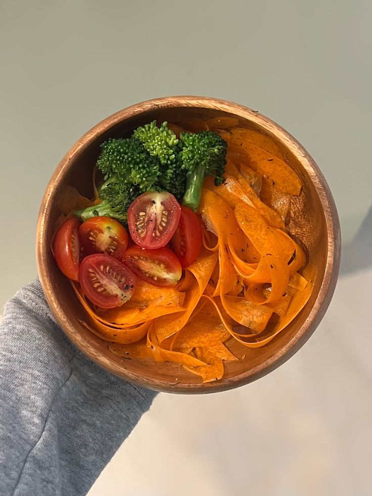 a wooden bowl filled with sliced up tomatoes and broccoli on top of a table