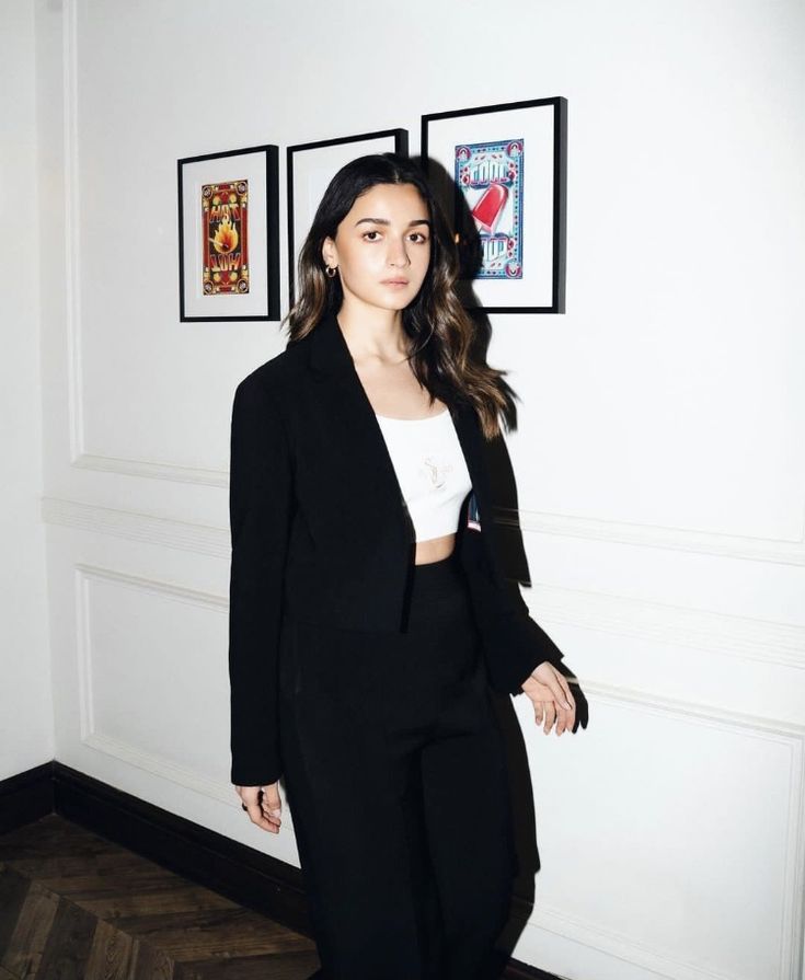 a woman in a black suit and white shirt standing next to a wall with pictures on it