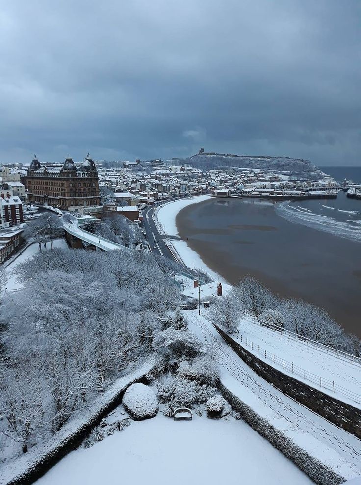 snow covered landscape with water and buildings in the background