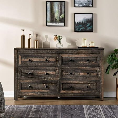 a wooden dresser sitting in a living room next to a wall with pictures on it