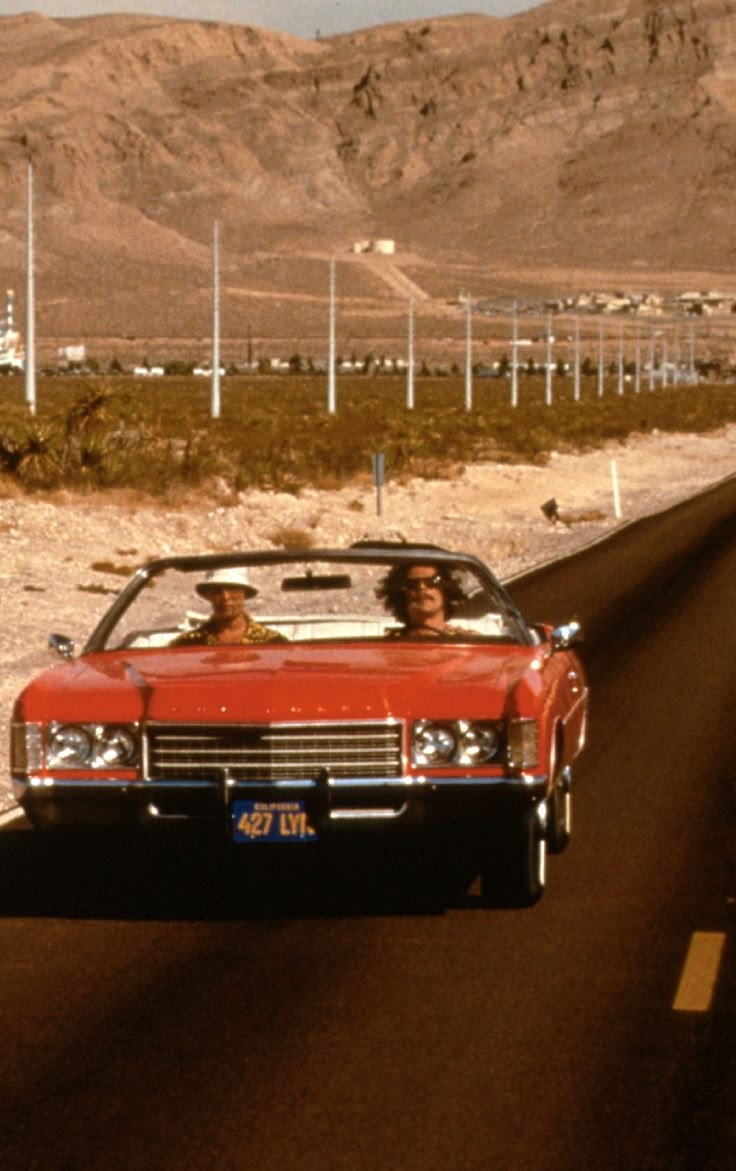 two people in a convertible driving down the road