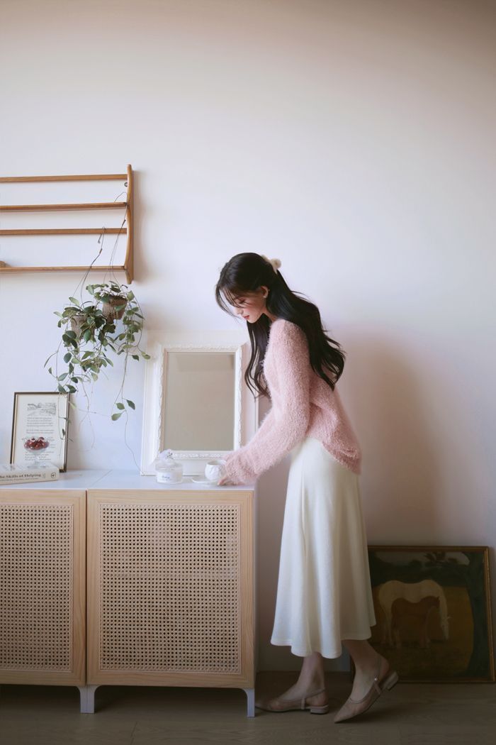 a woman standing in front of a dresser next to a plant