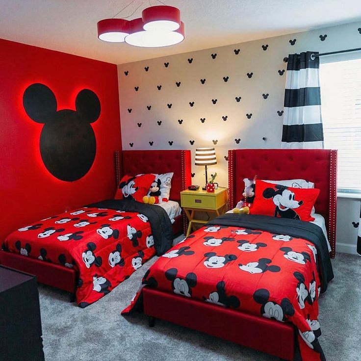 two beds in a room with mickey mouse decorations on the wall and red bedding