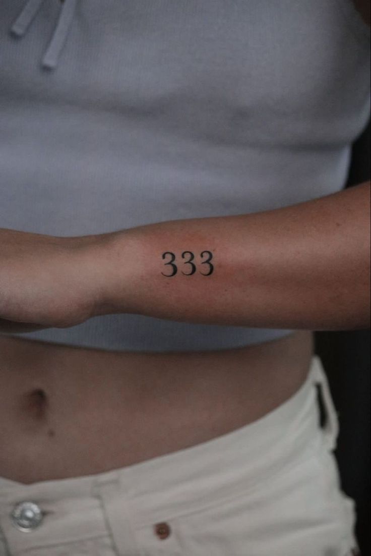 a woman's arm with the number 333 tattooed on her left arm, in black ink