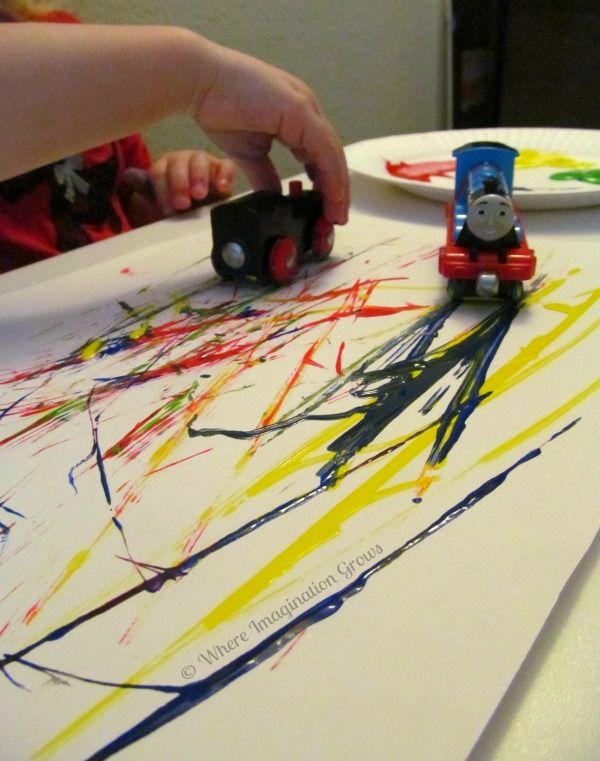 a child's hand is touching a train on a piece of paper with paint