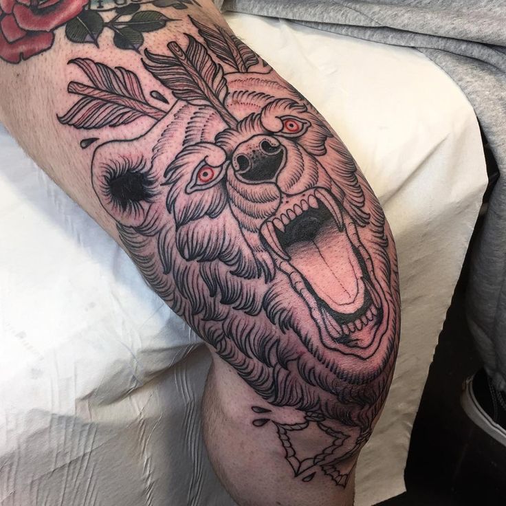 a man's arm with a bear and roses tattoo on it, sitting in bed