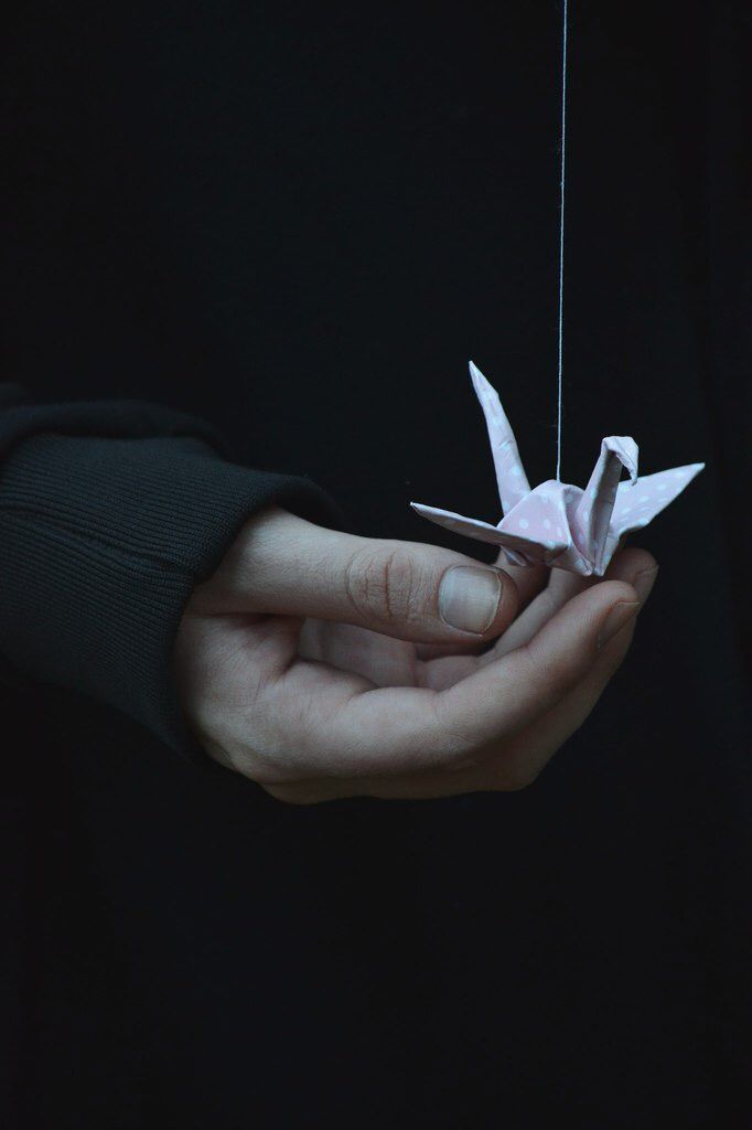 a person holding a white origami bird on a string in their left hand