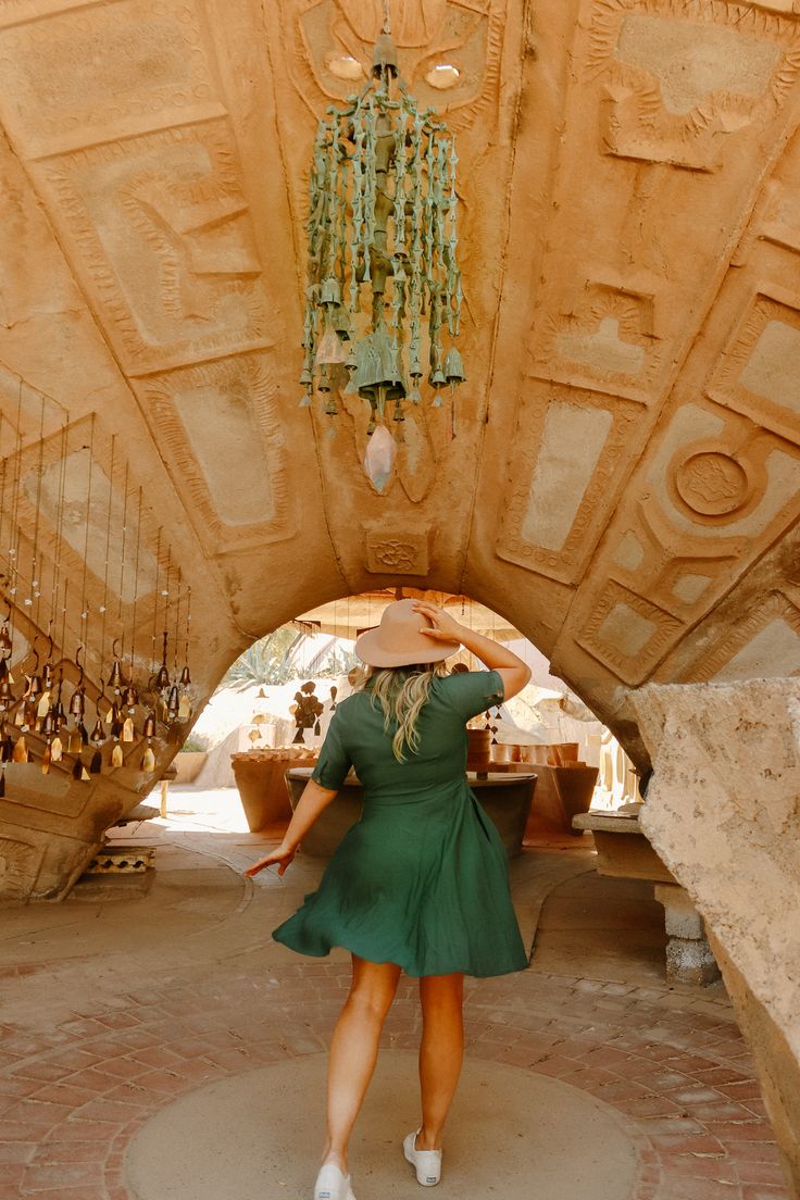 a woman in a green dress and hat walking through a tunnel with chandeliers hanging from the ceiling