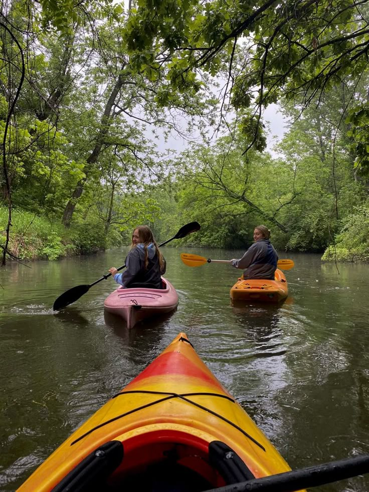 two people in kayaks paddling down a river surrounded by trees and greenery