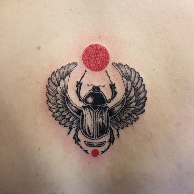 a beetle tattoo on the back of a man's upper chest with wings and a red ball