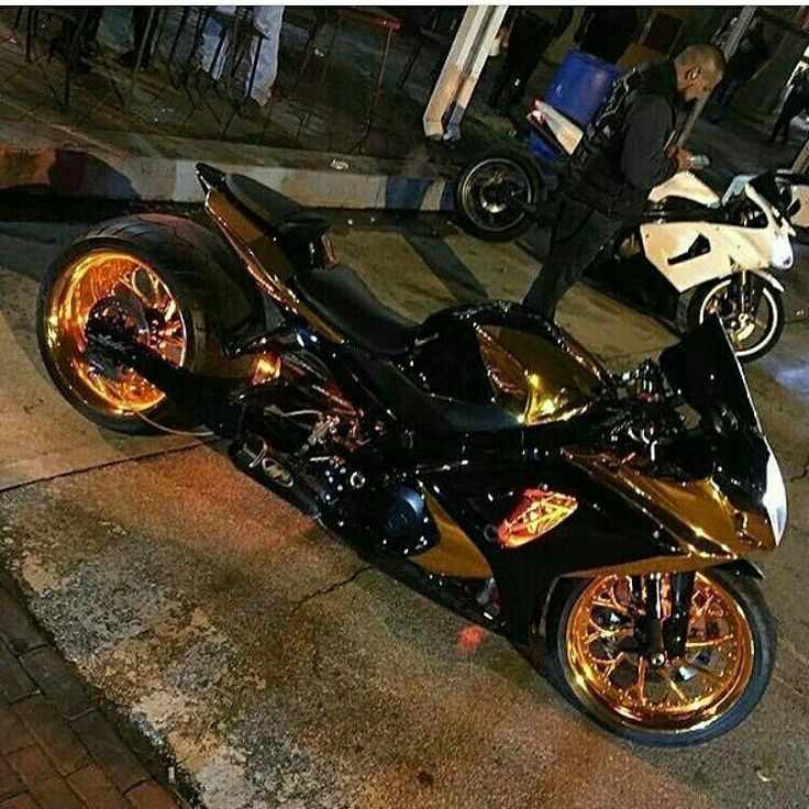 a gold and black motorcycle parked on the side of the road at night with people standing around