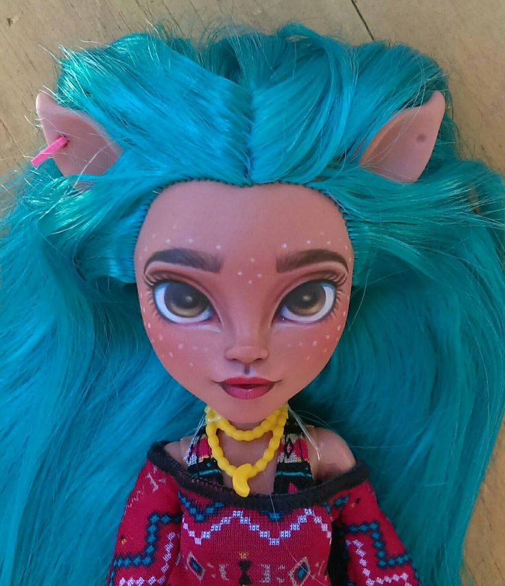 a close up of a doll with blue hair and big eyes on a wooden floor