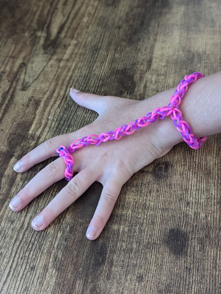 a child's hand wearing a pink bracelet with a cross design on it, sitting on top of a wooden table