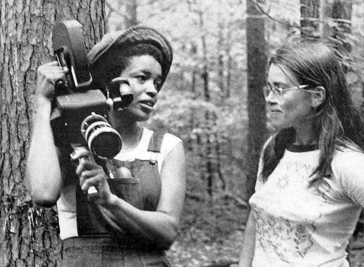 two young women standing next to each other in the woods with cameras on their shoulders