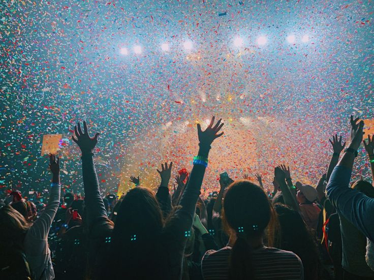 people at a concert with confetti falling from the ceiling and hands in the air