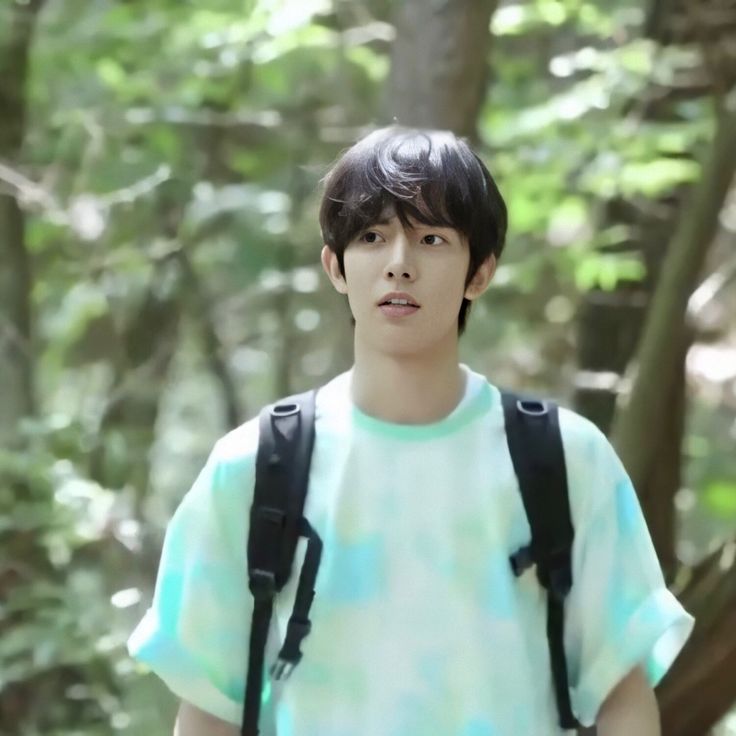 a young man wearing a backpack standing in the woods