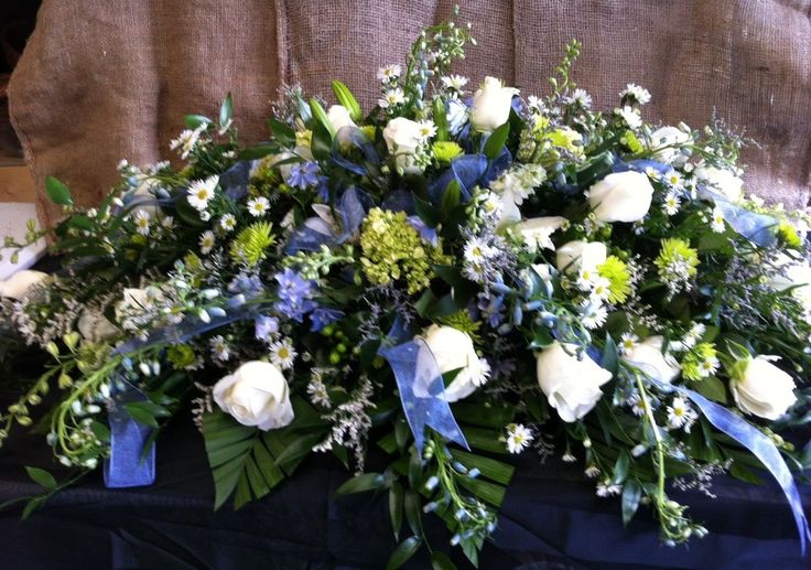 a bouquet of white roses and blue flowers on a black tableclothed cloth with green leaves