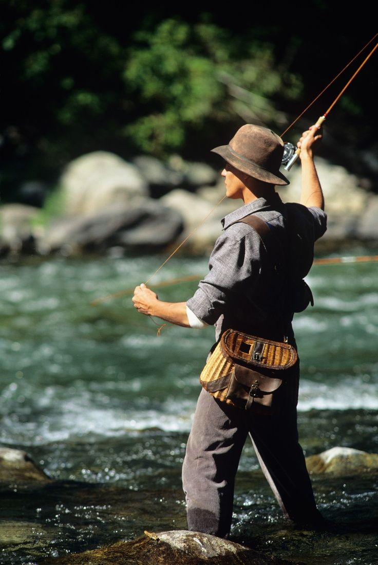 a man standing in the water while holding onto a fishing rod and wearing a hat