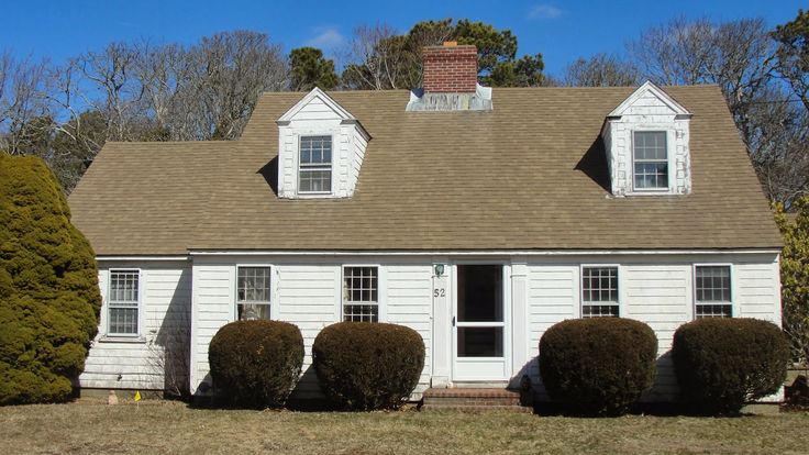 a white house with three windows and two bushes in front of it on a sunny day