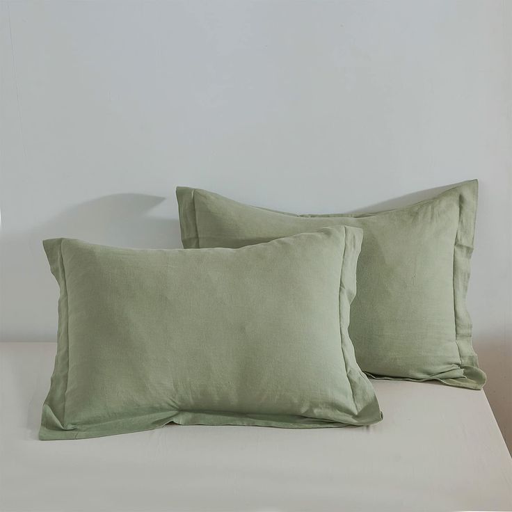 two light green pillows sitting on top of a bed next to a white headboard