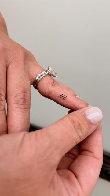 a woman's left hand with a ring on it and a cross tattoo on the middle finger