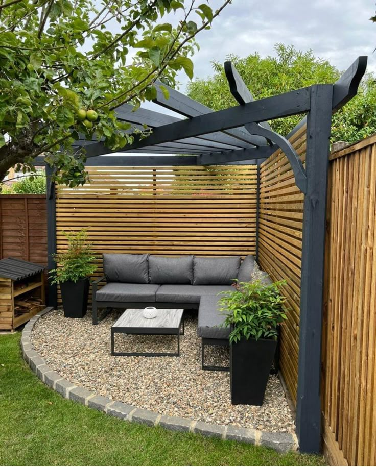 an outdoor seating area in the middle of a yard with wooden fence and plants on it