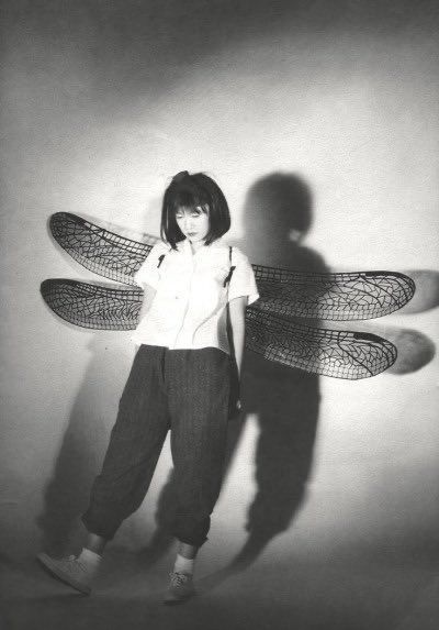 a black and white photo of a woman standing in front of a wall with dragon wings