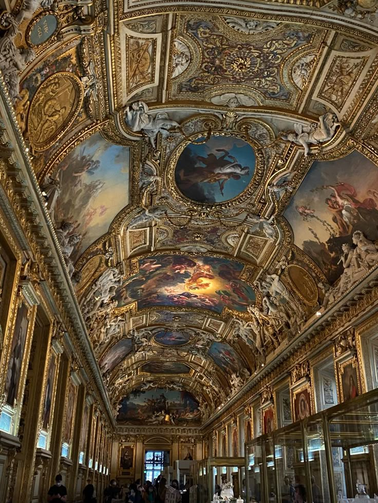 an ornate ceiling with paintings on it and people walking around in the room below them