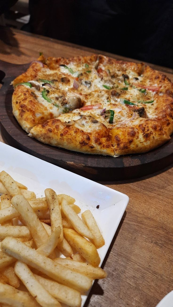 a pizza sitting on top of a white plate next to french fries in front of it