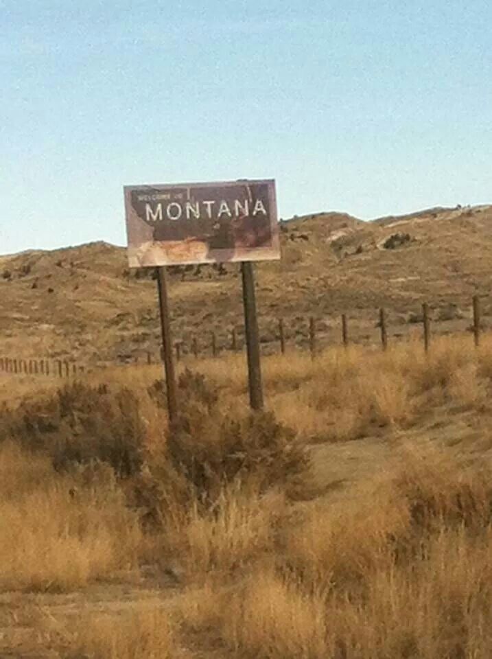 a sign that is on the side of a dirt road in front of a hill