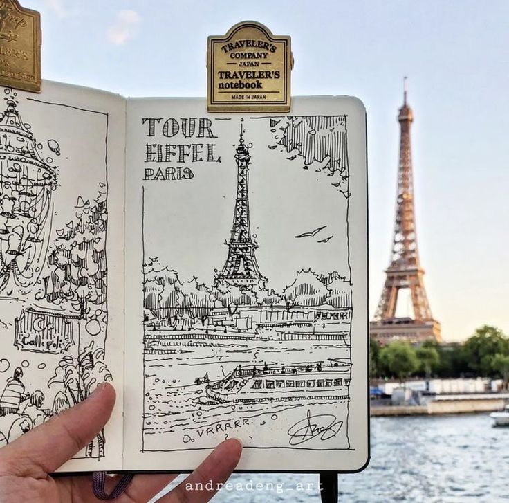 a hand holding up an open book with the eiffel tower in the background