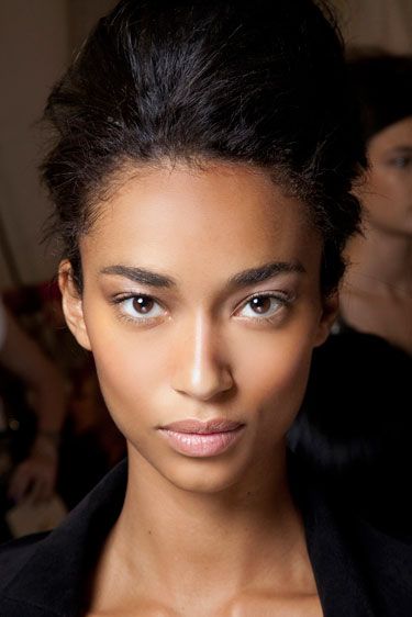 a close up of a person wearing a black shirt and jacket with hair in a bun