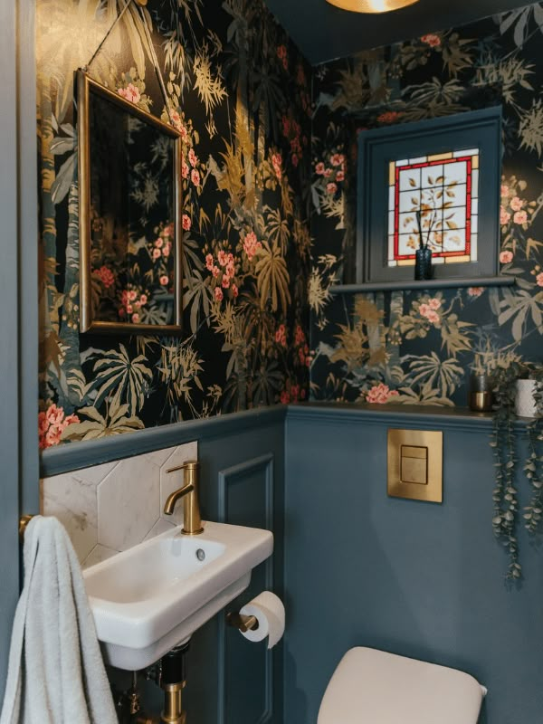 a bathroom with floral wallpaper and blue walls, gold fixtures and a white toilet