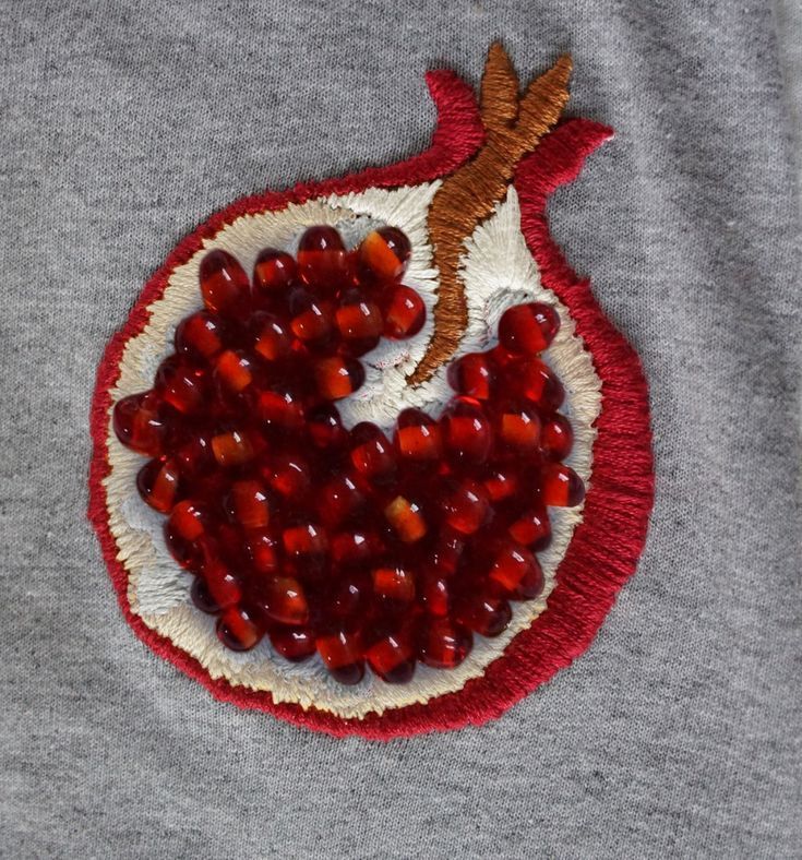 a close up of a pomegranate on a gray shirt with red trim