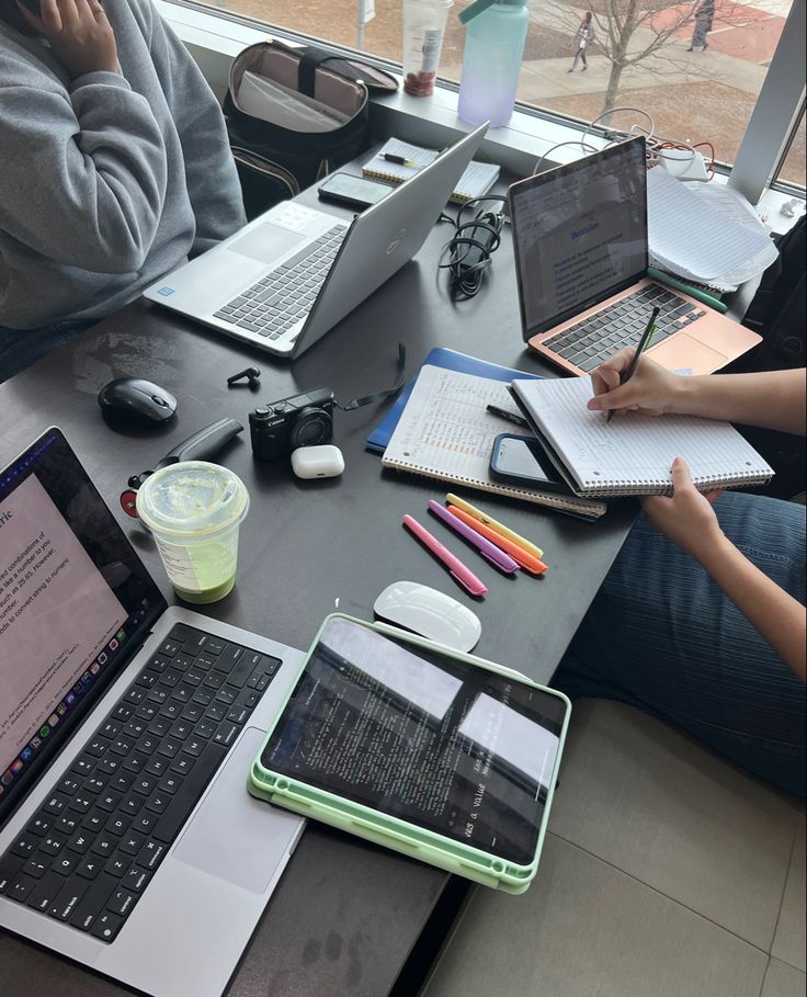 three people sitting at a table with laptops and notebooks