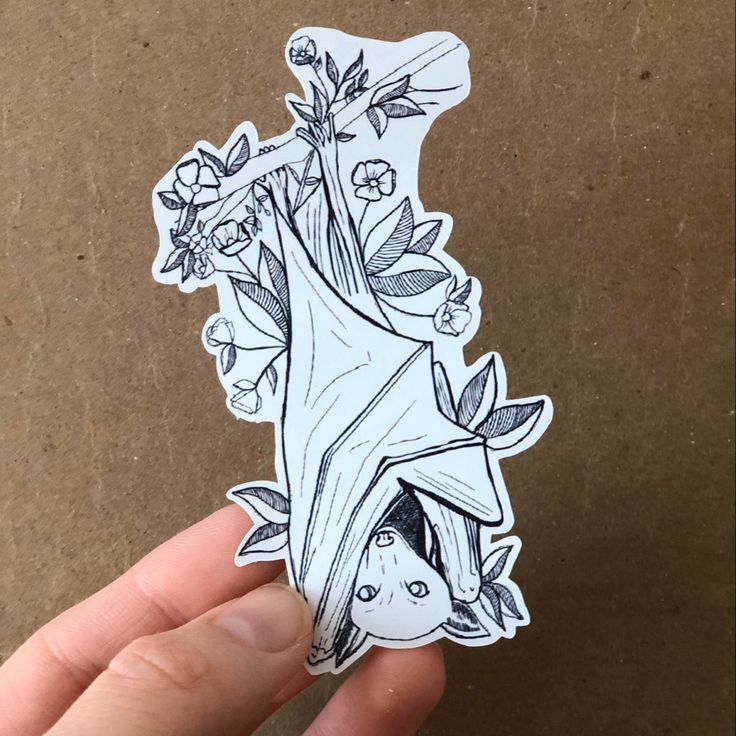 a hand holding a sticker with an image of a tree and flowers on it