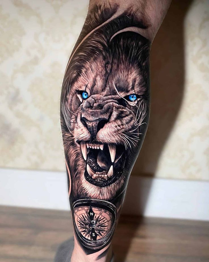 a man's leg with a lion and compass tattoo on his arm, which has blue eyes