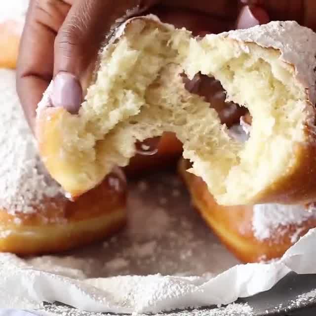 a person holding a doughnut with powdered sugar on it