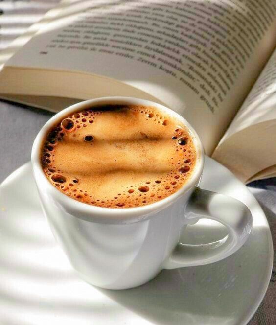 a cup of coffee on a saucer with an open book in front of it