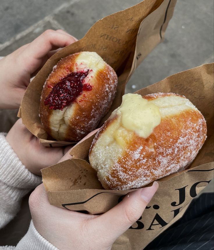 two people holding pastries in brown paper bags