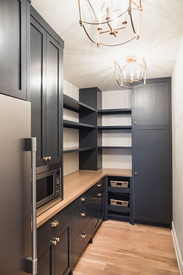 an empty kitchen with black cabinets and silver appliances in the corner, along with a chandelier hanging from the ceiling