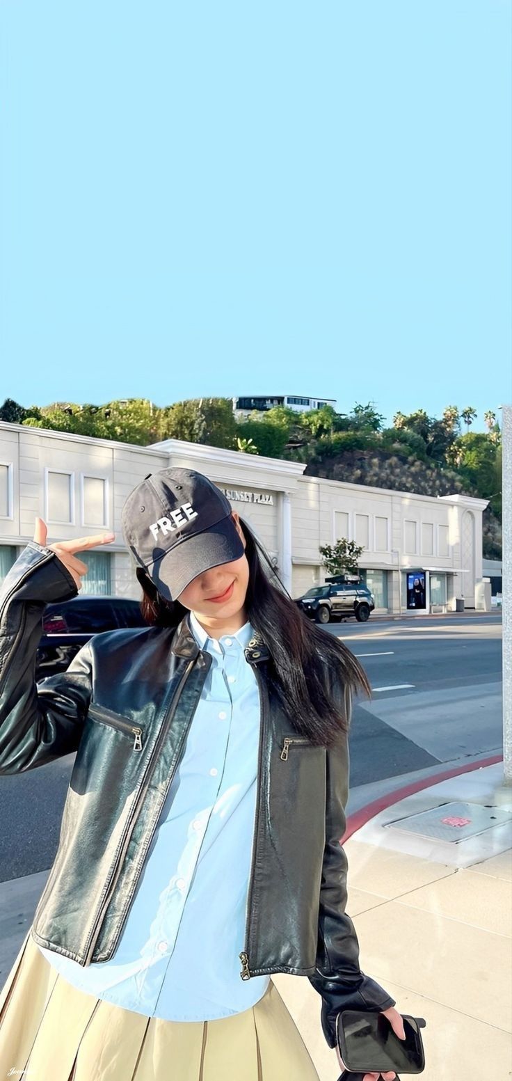 a woman wearing a hat and jacket is standing on the sidewalk with her hand in her hair