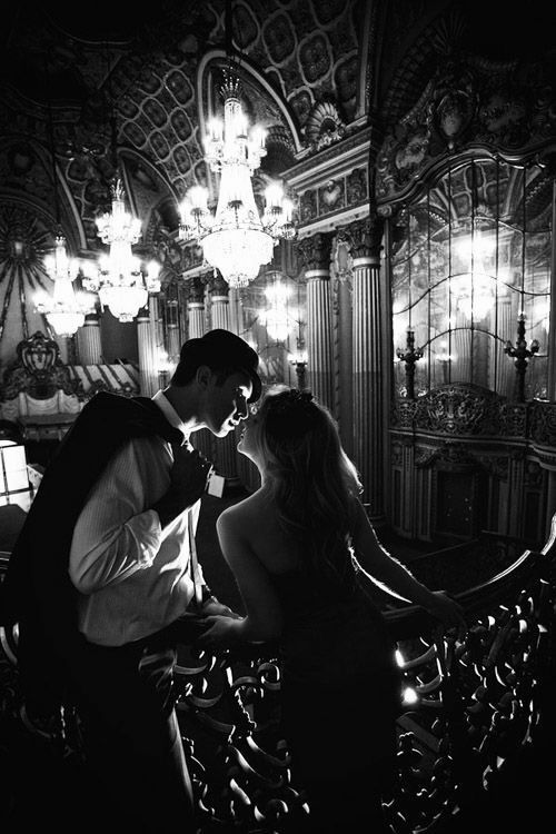 a man kissing a woman in front of a mirror with chandeliers hanging from the ceiling