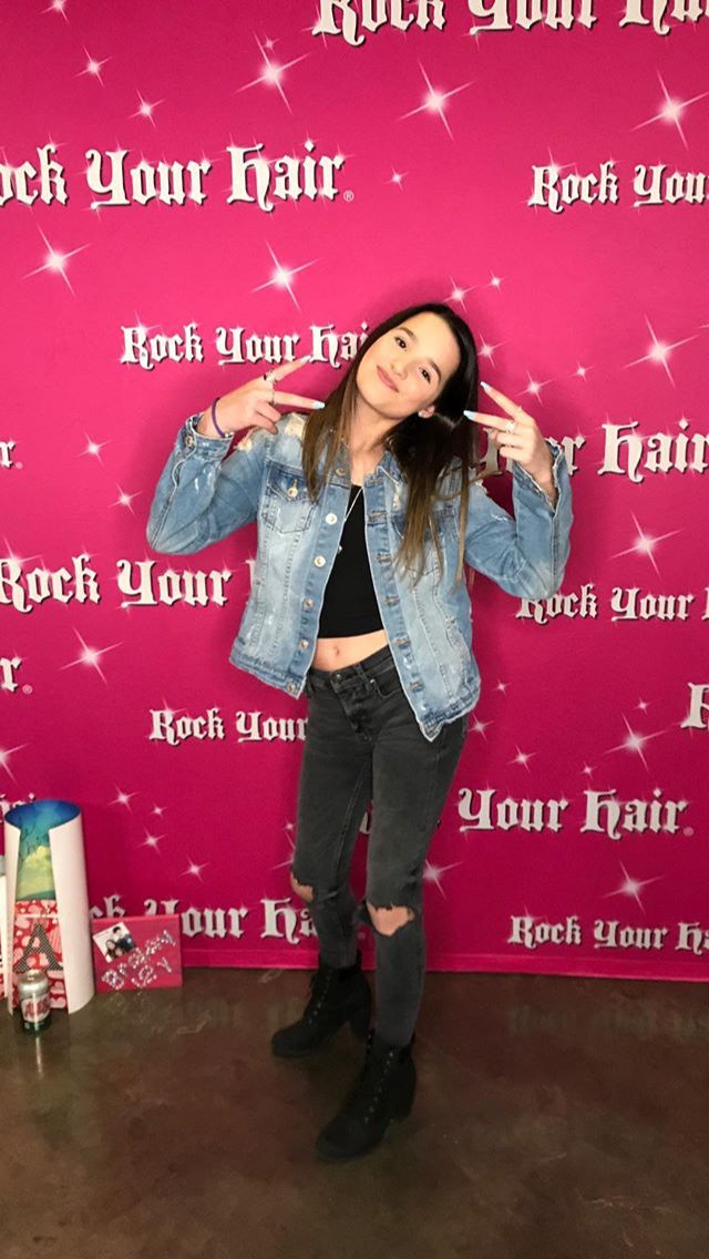 a woman standing in front of a pink backdrop with her hands up to the side