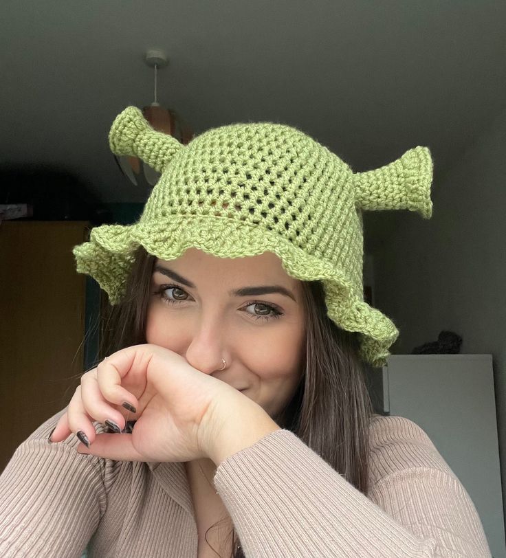 a woman wearing a green crocheted hat and smiling at the camera with her hand on her chin