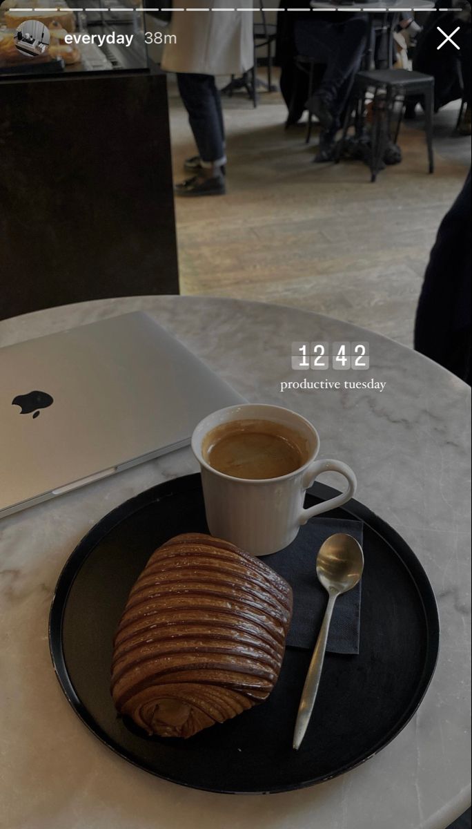 an apple laptop on a table with a cup of coffee and some croissants