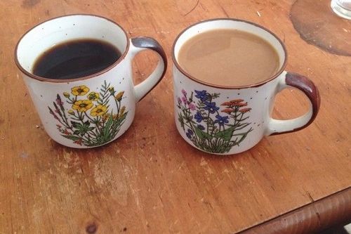 two cups of coffee sitting on top of a wooden table with flowers painted on them